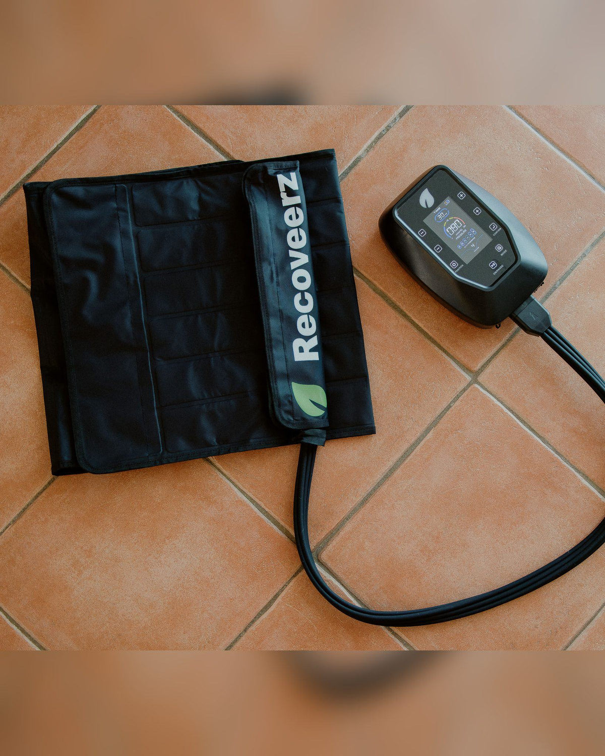 Ceinture de pressothérapie Recoveerz posée à plat avec son tuyau et son boîtier