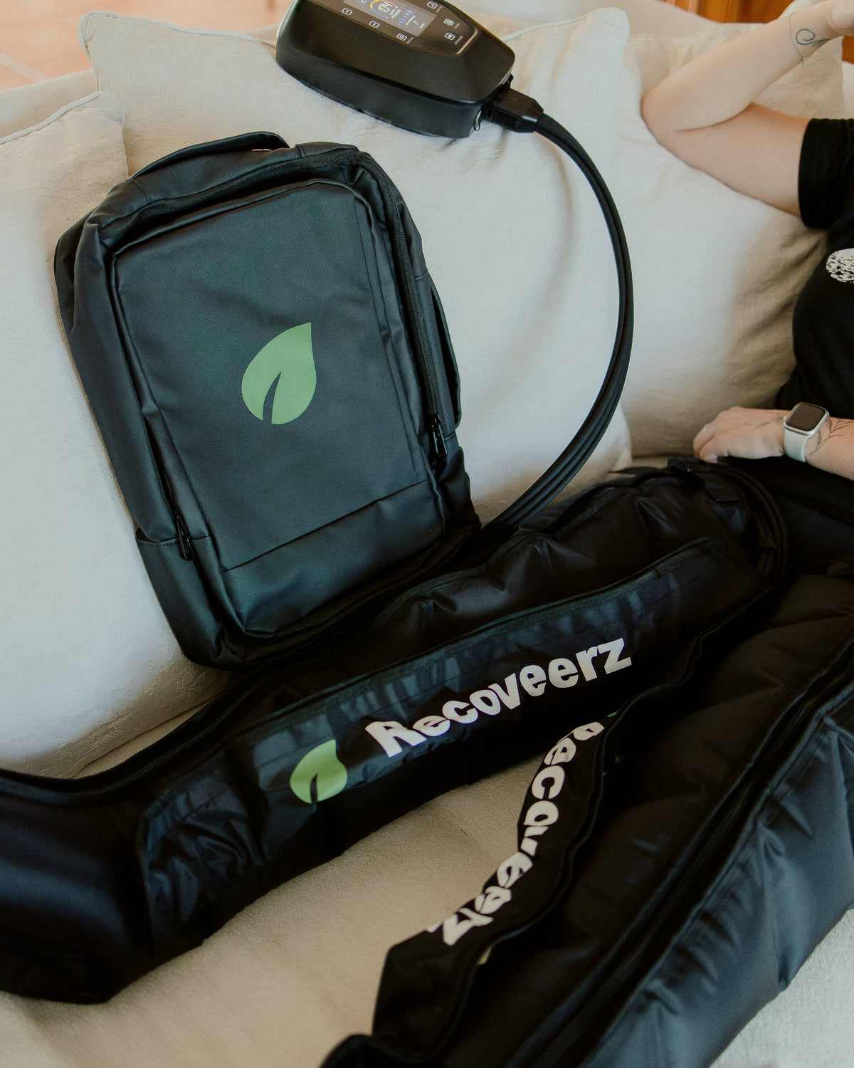 Sac à dos de transport Recoveerz inclus dans le pack, posé sur un canapé à côté des bottes de pressothérapie Recoveerz Pro 6 et de leur boîtier