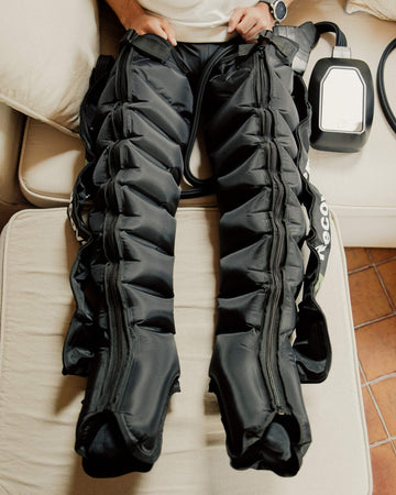Bottes de pressothérapie Recoveerz 8 chambres gonflées, portées sur un canapé, avec leur boîtier